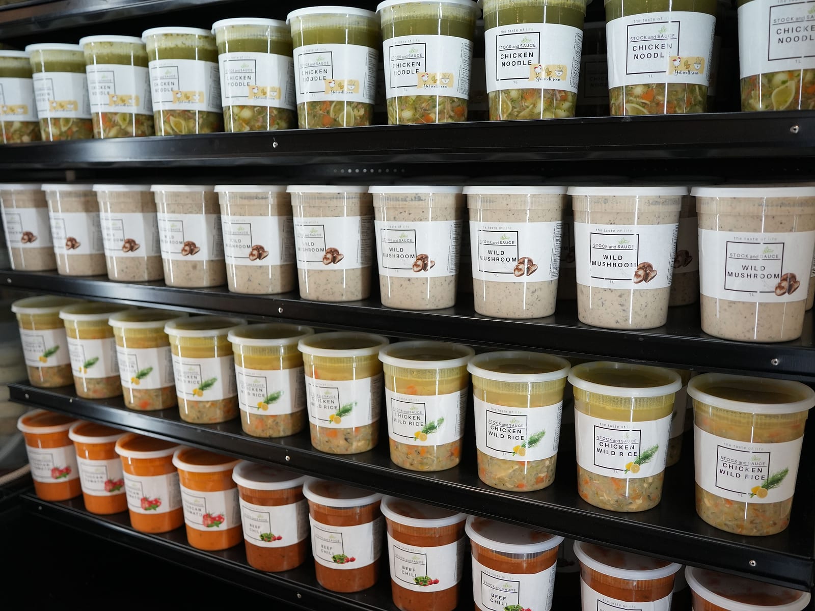Store fridge stocked with tubs of Thai chicken, Tuscan tomato and beef barley soup