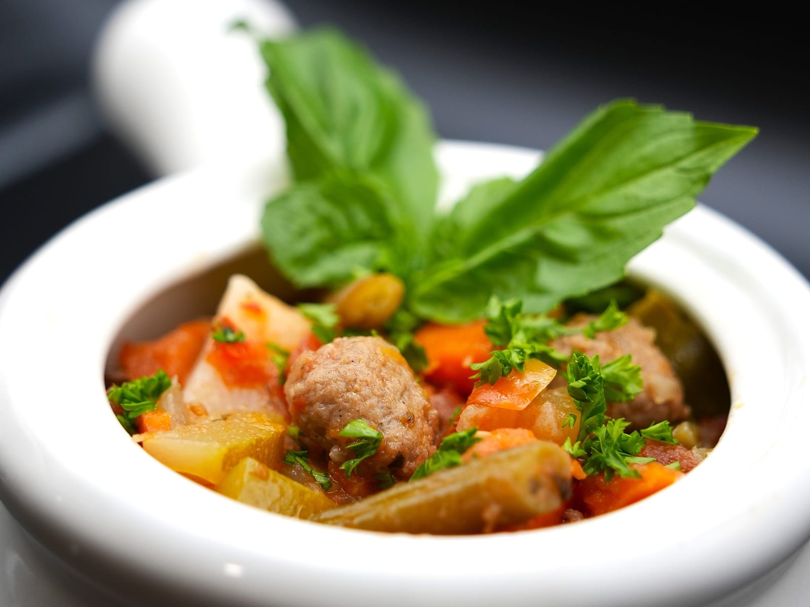Italian Meatball Stew served in a white crock, topped with fresh basil