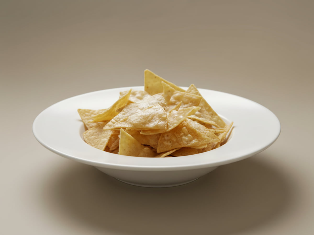 A bowl of golden corn tortilla chips, heaped and lightly salted