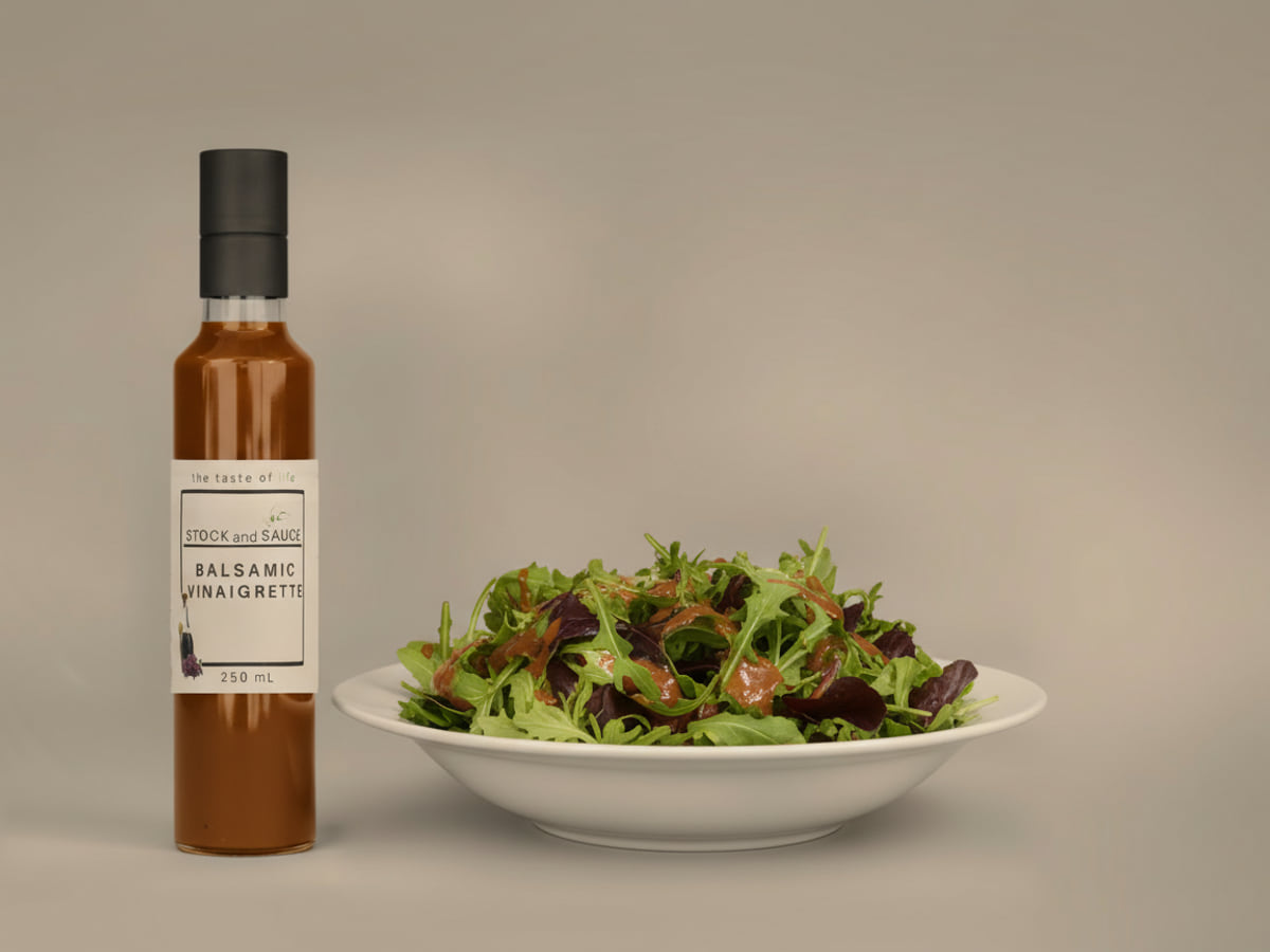 Bottle of Stock & Sauce Balsamic Vinaigrette beside a bowl of mixed leaves dressed with it