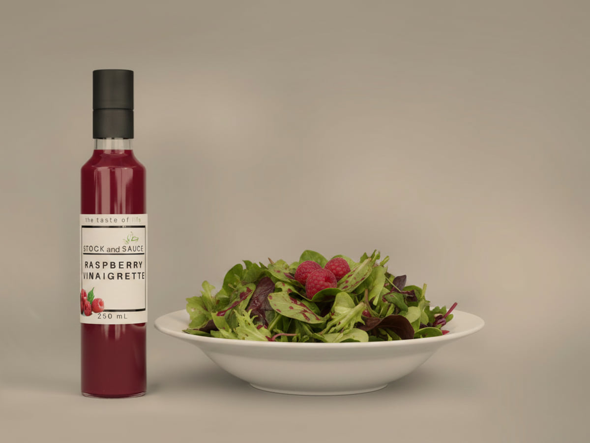 Bottle of Stock & Sauce Raspberry Vinaigrette beside a bowl of mixed leaves dressed with it
