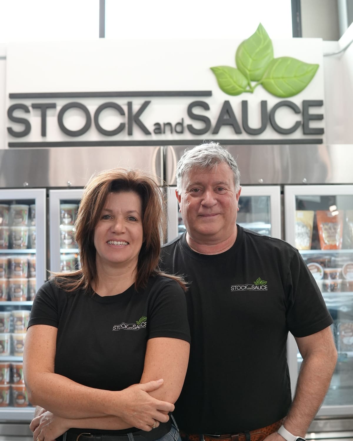 Kari and Phil Faba, owners of Stock & Sauce, in front of their market sign